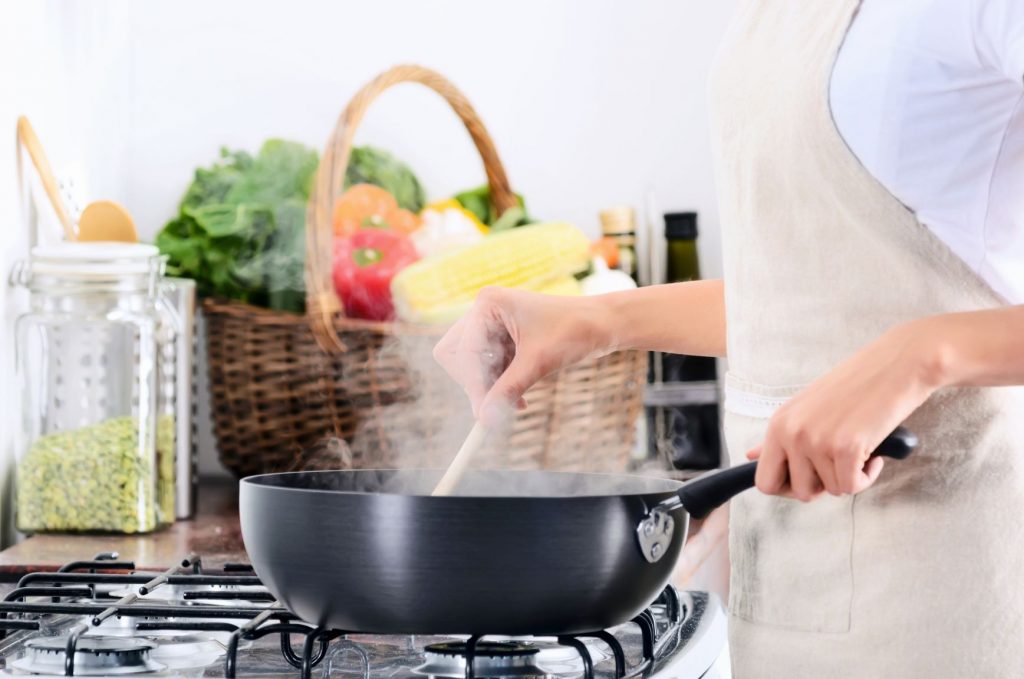 湯気の上がる鍋で料理する女性の手元