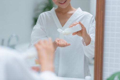 洗面台で鏡の前で手に化粧品をとる若い女性